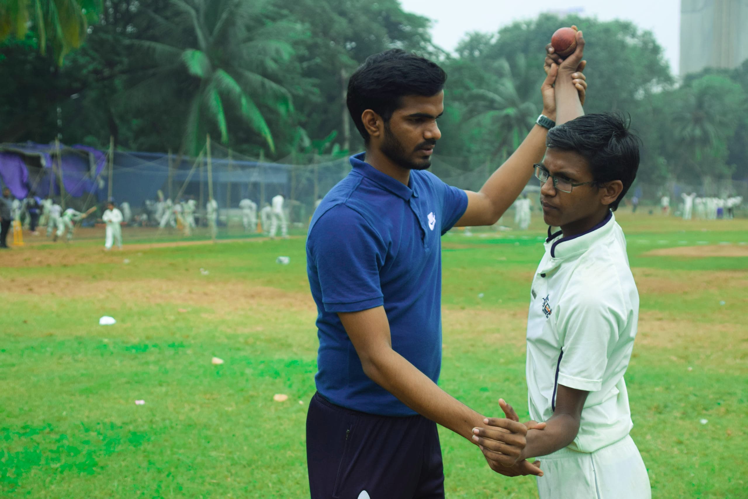 A coach guiding a young bowler through his bowling action