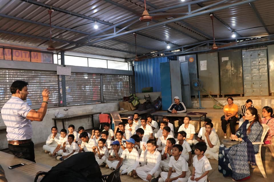 A speaker addressing academy players seated for an indoor session